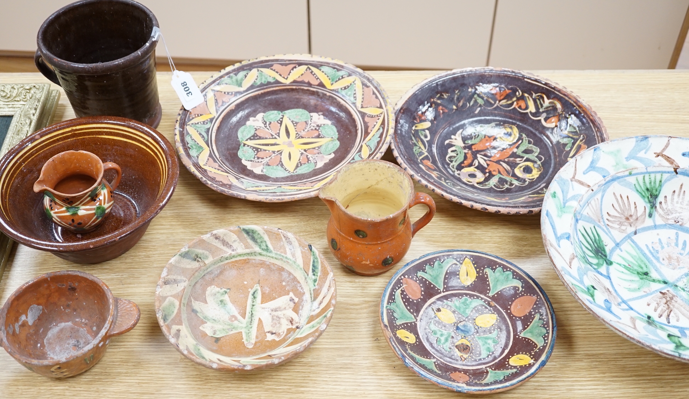 A group of Mediterranean slipware dishes, bowls and jugs, decorated in colours on a predominantly brown or ochre ground, the largest 33cm in diameter